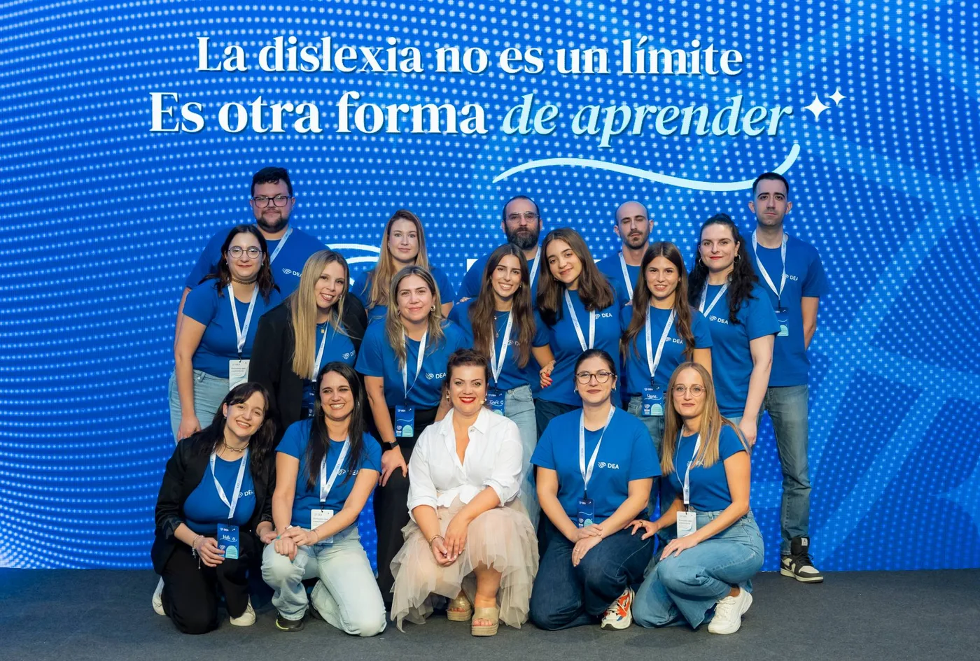 El equipo completo de Irene Dislexia Teacher con camisetas azules de DEA, posando delante de una pantalla con la frase «La dislexia no es un límite. Es otra forma de aprender»