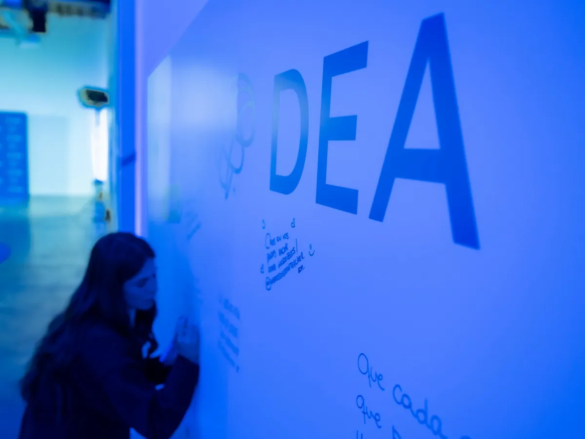Una alumna escribe un mensaje en un gran mural con las letras DEA, en un encuentro del Método DEA®